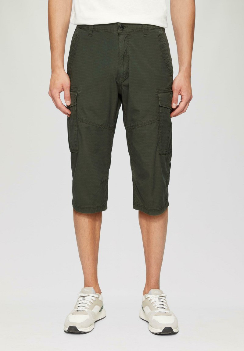 Cargo-Shorts aus dunkelgrünem Stoff, knielang, mit seitlichen Taschen, Reißverschluss und legerem Schnitt. Getragen mit hellgrauen Sneakers.