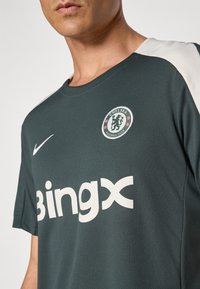 Mørkegrøn sportsjersey med Chelsea Football Club-logo, hvide detaljer på skuldrene og stort "Bingx"-tekst på forsiden.
