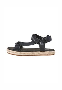 Musta nahkasaapas, jossa on espadrillo-tyylinen kudottu ina, säädettävät hihnat ja teksturoitu pohja mukavuutta varten.