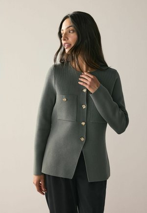 Grüner gerippter Blazer mit goldenen Blumenknöpfen, der über zwei Vorderaschen und einen geraden Schnitt verfügt. Weicher Stoff, lange Ärmel und maßgeschneiderter Schnitt.