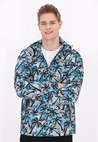 Jachetă ușoară cu glugă, având un model tropical de frunze în nuanțe de negru, alb și albastru. Fabricată dintr-un material respirabil, cu șnururi ajustabile.