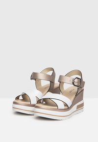White and metallic gold wedge sandals with cross straps, adjustable ankle strap, textured cushioned footbed, and layered sole design.