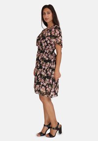 Vestido negro de flores con patrones de rosas rosas, mangas cortas, cintura elástica y dobladillo a la altura de la rodilla, combinado con sandalias de tacón alto negras.