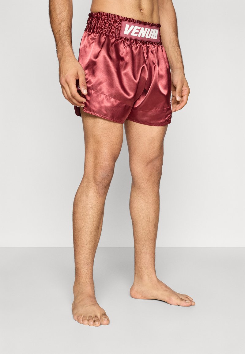 Sarkani atlasveida boksa šorti ar savākuma jostu un baltu logotipu. Šorti ir vidēja garuma līdz augšstilbam un izceļas ar gludu, spīdīgu tekstūru.