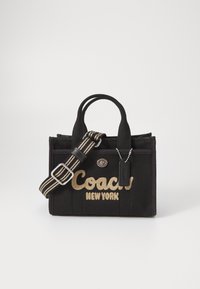 Crna platnena torba s zlatnim logotipom "Coach New York", dvostrukim ručkama, podesivim prugastim remenom, srebrnim hardverom i crnim oznakom kao naglaskom.