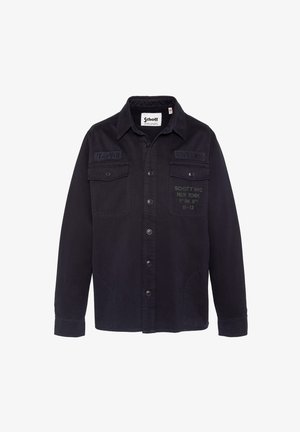 Chemise noire à boutons avec deux poches poitrine, patchs brodés indiquant "US740N" et "Schott NYC", et texte imprimé sur la poche droite.