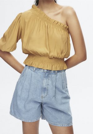 Mosterdkleurige off-shoulder top met volant halslijn, gecombineerd met hooggeritste lichtblauwe denim shorts met plooien en een relaxte pasvorm.