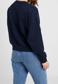Felpa blu navy con colletto rotondo, polsini e orlo a coste, abbinata a jeans a vita alta di un blu chiaro. Texture liscia e vestibilità comoda.