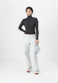 Grå ribbestrikket høyhalset genser kombinert med lyseblå vide jeans og bærer en sølvfarget veske. Skoene har røde detaljer.