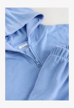 Világoskék cipzáras kapucnis pulóver puha anyagból, kapucnival és gumírozott mandzsettákkal. A cipzár megkönnyíti a viseletet. Címke látható.