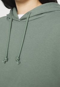 Grön bomullshoodie med en framficka i kängurustil, justerbara dragsko och en mjuk textur. Har en avslappnad, oversized passform.