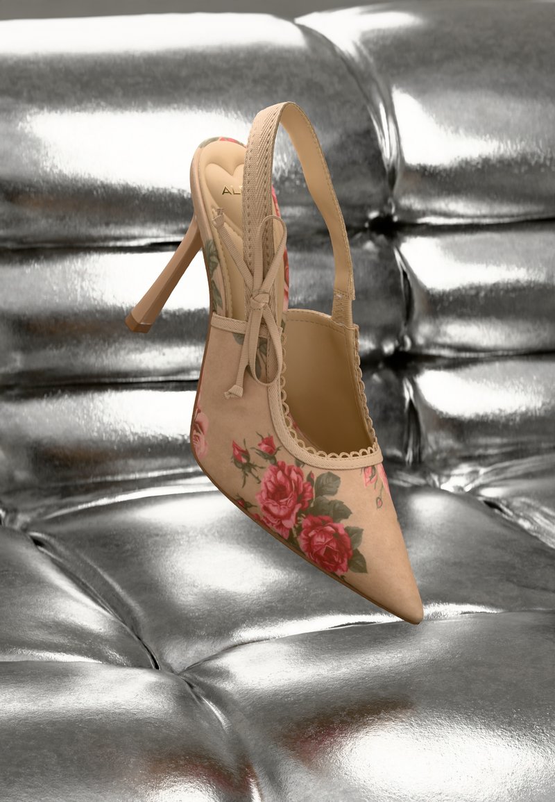 Zapato stiletto con tira trasera en ante beige con estampado floral rosa, punta picuda y ribete de encaje. Fondo plateado brillante.