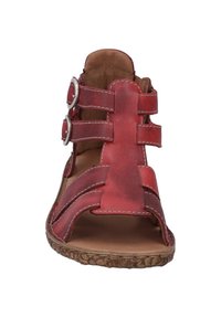 Rode leren sandaal met open teen en uitsnijdingen, voorzien van twee verstelbare banden met zilveren gespen en een getextureerde bruine zool.