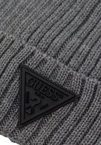 Bonnet tricoté gris avec une texture côtelée et un patch logo triangulaire noir comportant du texte embossé et des détails de logo.