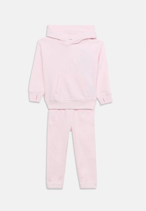 Completo due pezzi per bambini rosa chiaro con felpa con cappuccio e pantaloni abbinati su sfondo bianco semplice.