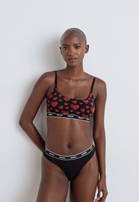 Svart bralette med rødt hjerteprint og tynne stropper; matchende svart truse med hvit logo på midjebåndet; glatt stoff; tettsittende design.