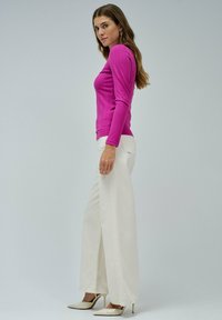Top de manga larga ajustado y acanalado en un brillante color rosa, combinado con pantalones anchos de un blanco crema y tacones de punta beige.