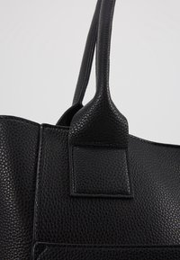Gros plan d’un sac à main en cuir noir texturé montrant la fixation de la anse et les détails de la couture.