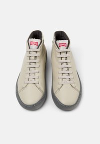 Zapatillas altas de cuero beige con suelas de goma gris, con cordones planos, un zip lateral y el logo de la marca en rojo en la lengua.