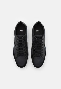 Schwarze Sneakers aus einer Mischung aus strukturierten und glatten Materialien, mit sechs Ösen, einem Logo auf der Zunge und einer Gummisohle.