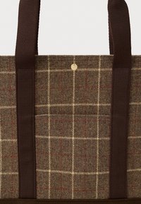 Τσάντα ώμου από καφέ ύφασμα, με καρό σχέδιο σε μπεζ και κόκκινες αποχρώσεις, με σκούρους καφέ ιμάντες, μπροστινή τσέπη και μικρό στρογγυλό μεταλλικό κουμπί στο κέντρο. 