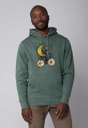 Grüne Kapuzenjacke mit einem Frontdruck eines Cartoon-Bananas, die ein Fahrrad fährt. Hergestellt aus einem weichen Material, mit einer Kängurutasche und verstellbaren Kapuzenzugbändern.