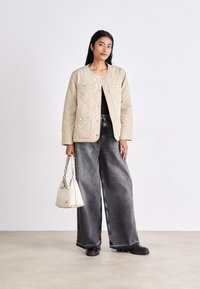 B�ēšs quiltēts jaka ar pogām un divām priekšējām kabatām, apvienota ar platām, izbalējušām melnām džinsa biksēm un mazu baltu rokassomu.