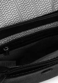 Schwarze Tascheninnenseite gezeigt, mit einer strukturierten Stoffauskleidung im Zickzackmuster und mit Reißverschlussfächern zur Organisation.