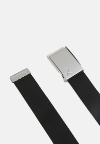 Svart elastisk bälte med en silverfärgad metallspänne som har en logotyp. Har en texturerad yta och en rektangulär, minimalistisk design.