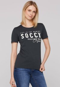 Camiseta de algodón negra con cuello redondo y mangas cortas. Texto blanco impreso que dice "SOCCX" y "MARCA REGISTRADA Originals."