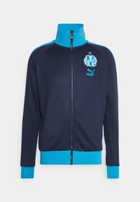 Marinblå zip-up jacka med turkosa detaljer på kragen och ärmsluten. Har en logotyp på bröstet och en klassisk atletisk design.