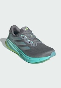 Scarpa sportiva grigia con tomaia in rete traspirante, dettagli in teal e tre strisce laterali. Presenta una soletta imbottita per il comfort.