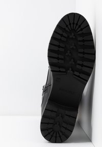 Black ankle boot with a textured surface, rubber sole featuring a rugged tread pattern, and a side zipper for easy wear. Brand name embossed.