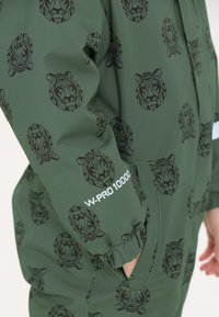 Groene waterdichte overall met een geometrisch leeuwenpatroon in het zwart. Kenmerken zijn onder andere elastische manchetten en een "W-PRO 10000" label op de mouw.
