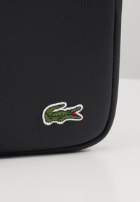 Custodia nera con texture e bordi arrotondati, caratterizzata da un logo di coccodrillo verde con dettagli rossi, ricamato sul fronte.