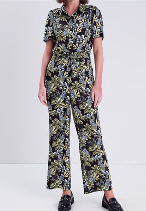Combinaison florale noire avec imprimé botanique vert et bleu, manches courtes, taille nouée, et design à jambes larges. Texture de tissu lisse.