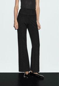 Zwarte wijde broek gemaakt van textuurstof, met een hoge taille en contrasterende naden, gecombineerd met zwarte loafers.