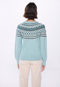 Jasnoniebieski sweter z dzianiny z wzorzystym yoke w kolorze kremowym i ciemnoniebieskim. Posiada długie rękawy oraz ściągacz na dole, wykonany z miękkiego, teksturowanego materiału.