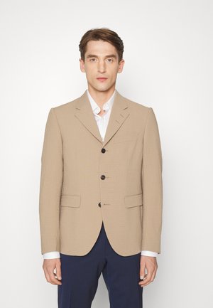 Blazer texturizado bege com lapelas em notched, dois bolsos frontais, fecho de três botões e botões escuros em contraste, usado sobre uma camisa branca.