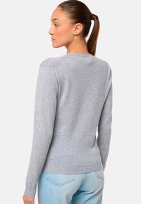 Hellgrauer Strickpullover mit rundem Halsausschnitt, langen Ärmeln, taillierter Passform und geripptem Saum. Getragen mit hellblauen Jeans.