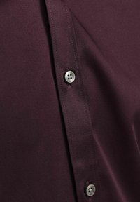 Bordeaux overhemd met een gladde stof, knoopdetail met een viergaatjes zilveren knoop en een schone, op maat gemaakte snit.
