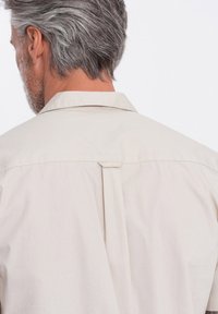 Hellbeige Hemd mit klassischem Kragen, Rückenpasse und Falten für Bewegungsfreiheit sowie einer weichen, glatten Stoffstruktur.