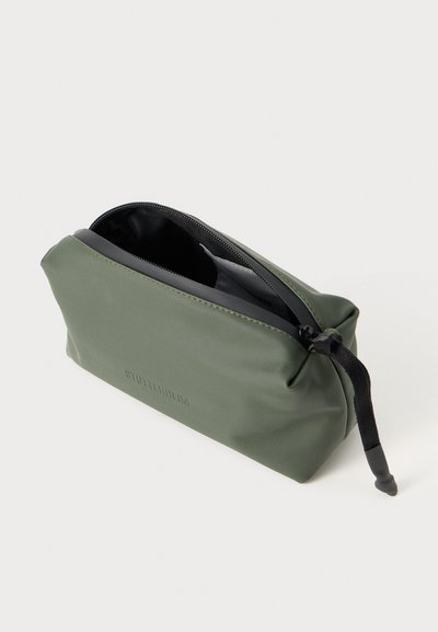 Borsa cosmetica impermeabile verde con chiusura zip e fodera nera. Presenta una texture morbida e opaca e un logo in rilievo sul lato.