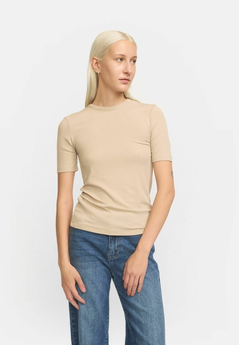 Beige bordázott póló, rövid ujjú, kerek nyakkivágással, testszínhúzó fazonban. Közepes mosású, laza farmernadrággal viselve, minimális részletekkel, sima textúrával.