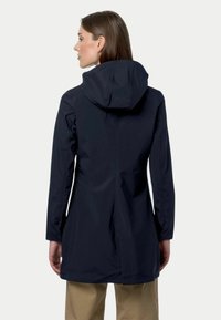 Veste imperméable navy avec capuche, manches longues et coupe droite. Présente une texture lisse et une fente dans le dos pour une meilleure respirabilité.