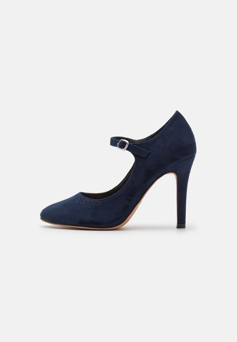 Chaussure à talon haut en daim bleu marine avec un bout arrondi, une lanière autour de la cheville et des détails perforés le long du bord. Talon fort et fin.