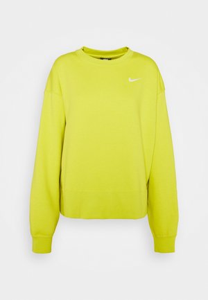 Jasnożółta bluza Nike z długim rękawem, okrągłym dekoltem i małym białym logo Swoosh na górnej lewej części klatki piersiowej, prezentowana na białym tle.