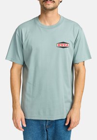Light blue cotton t-shirt with short sleeves, featuring a red and black RVCA logo patch on the left chest area. Smooth texture, relaxed fit.