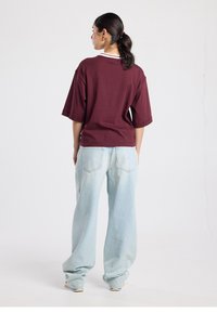 T-shirt oversize marron avec manches courtes et col blanc, associée à un jean denim bleu clair à jambes larges avec poches arrière.