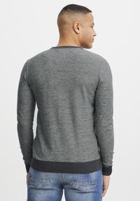 Gray knit sweater with long sleeves, round neckline, textured fabric, and ribbed cuffs and hem, paired with blue denim jeans.